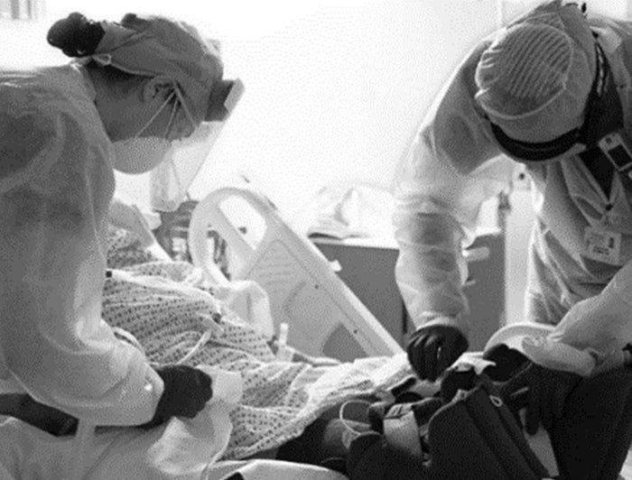 Doctors in PPE attend to patient in hospital bed