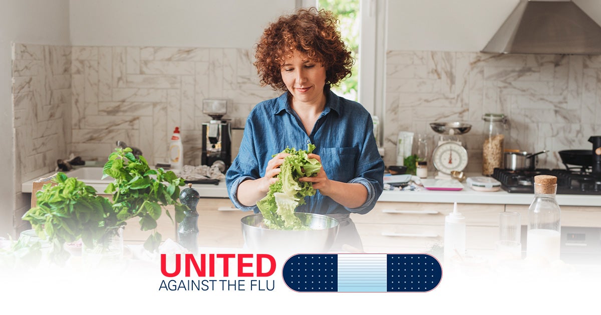 united against the flu - curly brunette woman preps lettuce for salad in a luxury kitchen