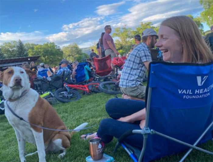 Woman with dog by her side sits in vail health branded lawn chair at an outdoor event