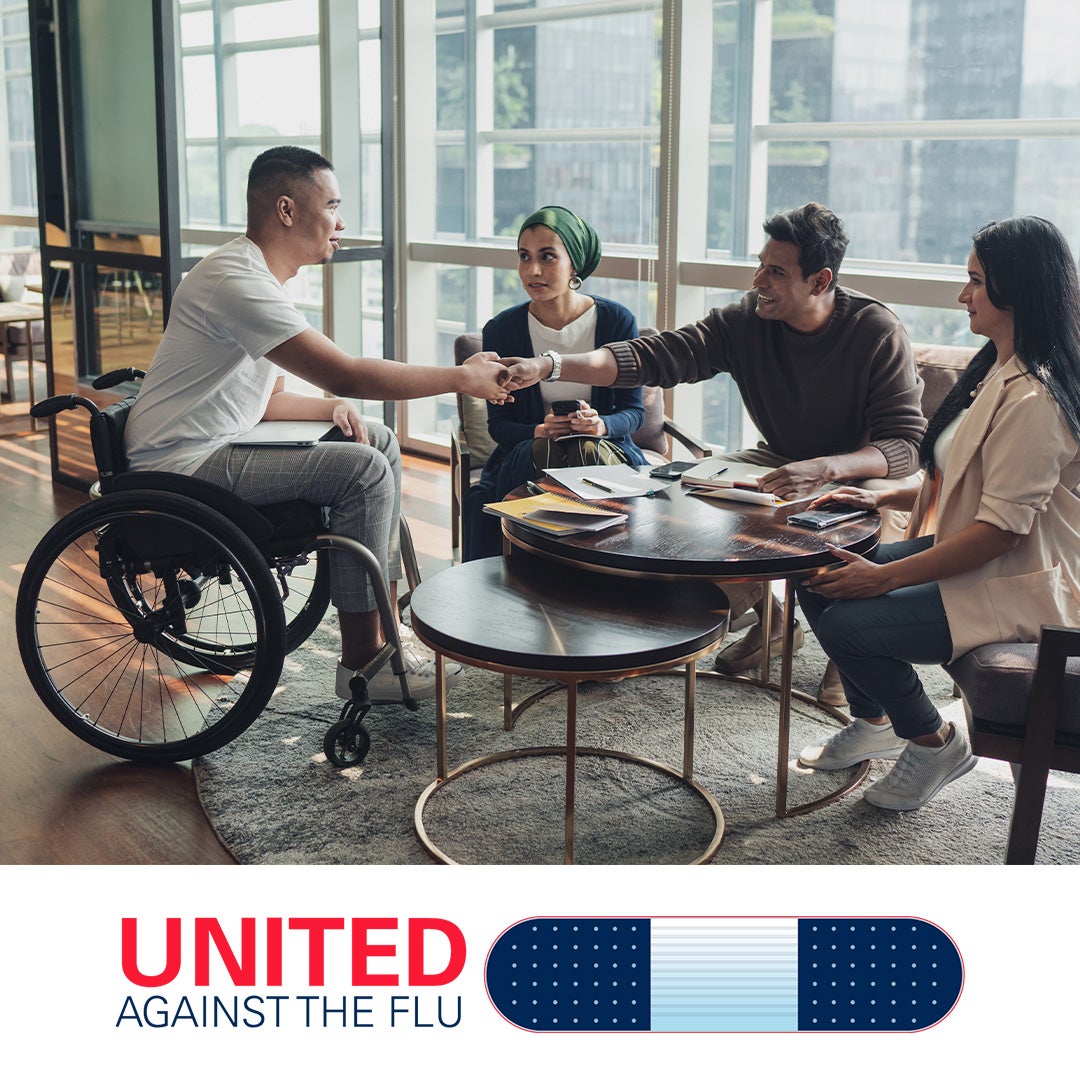 Diverse group of young adults sits around a cafe table with notepads and files on it. Three sit on one side. The fourth, a man in a wheelchair, shakes hands with one of the three as though it is a first meeting or interview. United Against the Flu logo at bottom of image