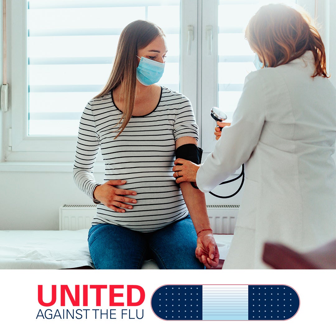 Pregnant white patient with long hair, wearing mask and striped shirt, sits on exam table while health worker in white coat checks blood pressure. United Against the Flu logo at bottom of image