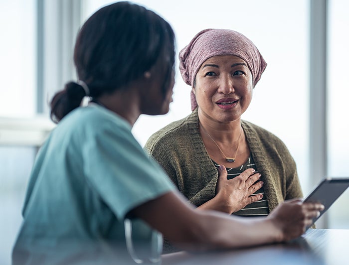 female health worker holding tablet talks with female patient wearing scarf on her head