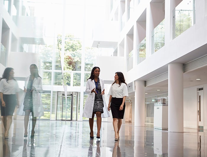 stock image of a female physician and female executive talking in a hispital atrium