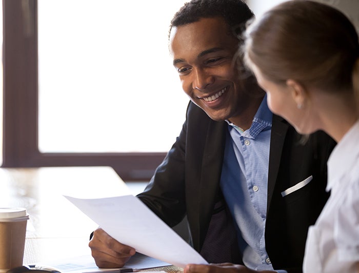Black businessman smiles while reviewing paperwork with colleague facing away from camera