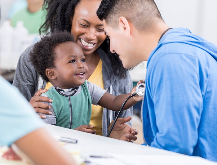 mother and doctor smile while baby plays with stethoscope