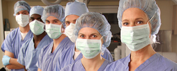 Learn Proven Strategies to Navigate Today’s Nursing Workforce. A row of diverse nurses in scrubs, bouffant caps, gloves, and surgical masks.
