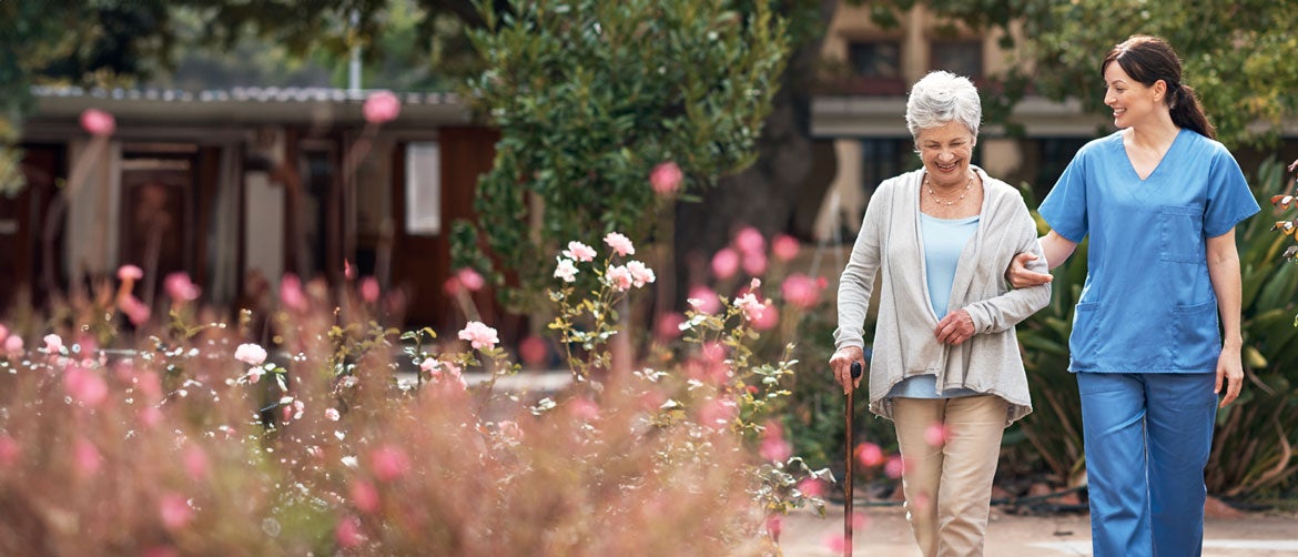Older person walking with medical staff outside among flowers