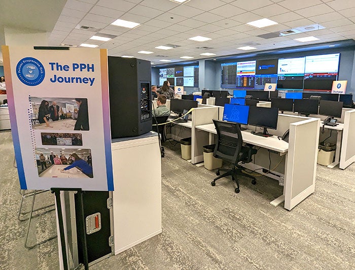 Photo of the Patient Progression Hub shows cubicles facing wall of screens