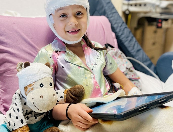 A young patient sits upright in a hospital bed holding an iPad