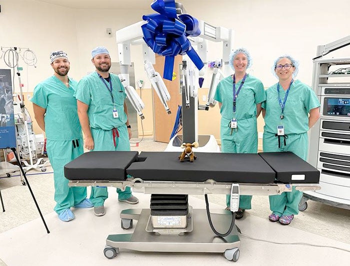 Intermountain robotic surgery team poses with da Vinci device and a stuffed moose on an operating table