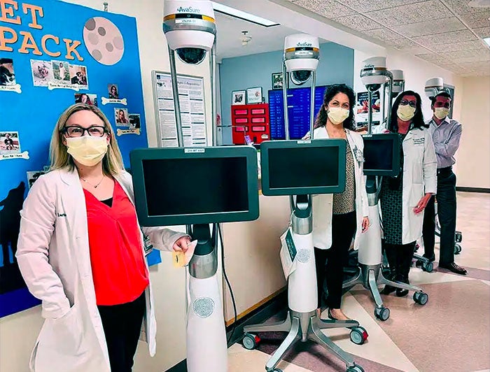 health workers wearing surgical masks stand lined up beside virtual nurse mobile telehealth units