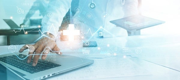 Explore Reinvention to Build a Future-Ready Workforce. A clinician holding a tablet types on a laptop keyboard with analytics data displaying as an overlay on the image.