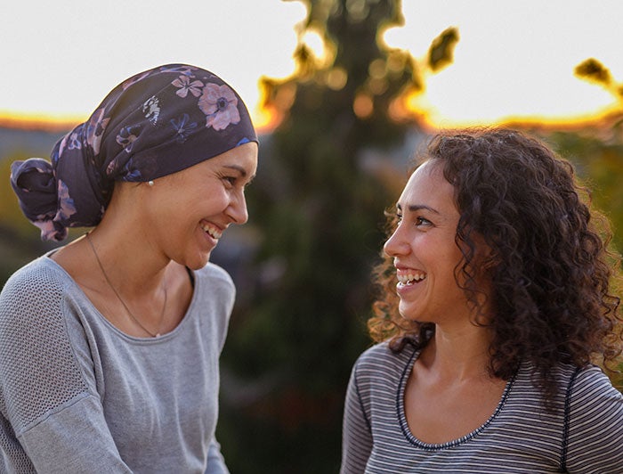 Two smiling women, one wearing a head scarf, sit outside at sunset