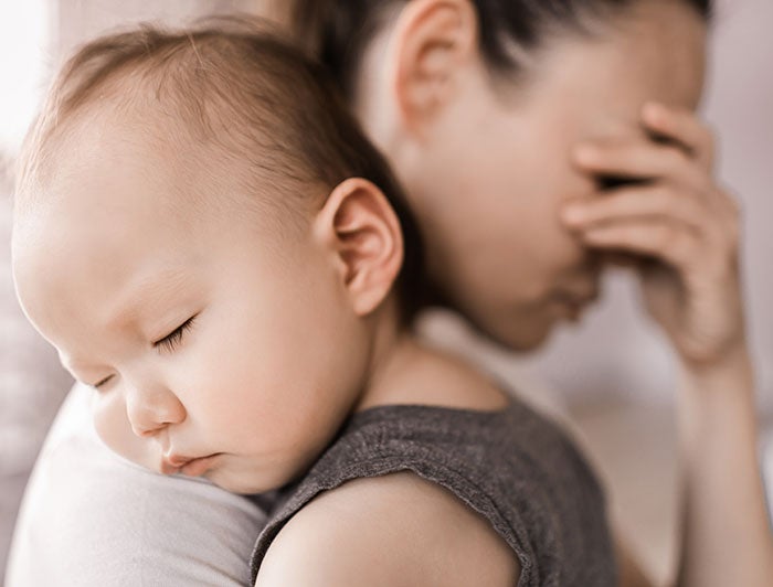 Stock photo: A woman holding a sleeping baby over her shoulder covers her own eyes in distress