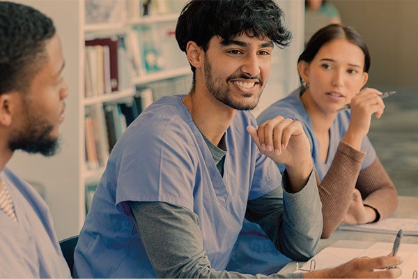 young people in scrubs and white coats sit talking in a row