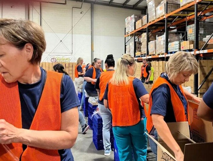 Reading Hospital. People wearing orange vests in a warehouse stand while packing boxes.
