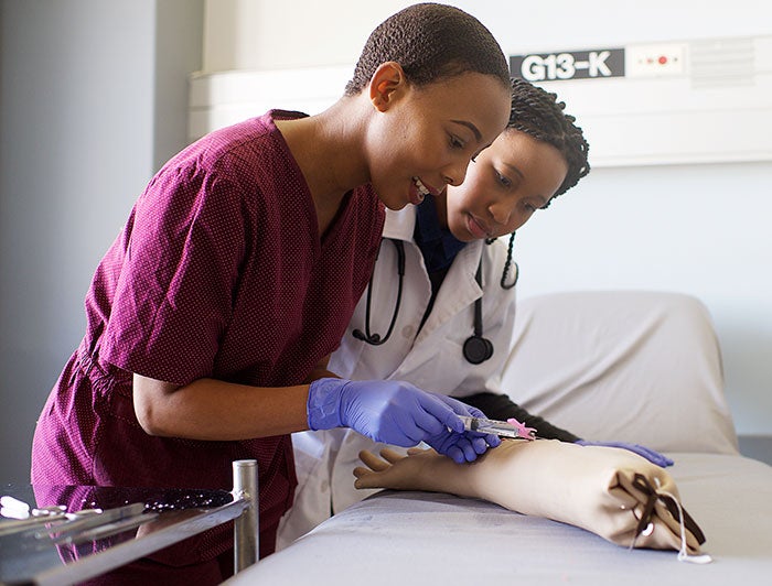 UMass Memorial Health. Female clinician uses prosthetic arm to demonstrate IV insertion to a trainee