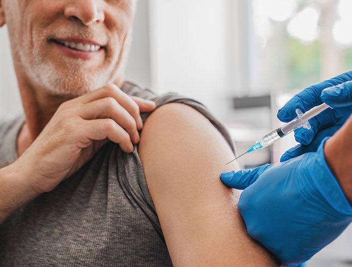 Telling the Hospital Story: Wallowa Memorial Hospital. An older man sits smiling while gloved hands administer vaccine in his arm