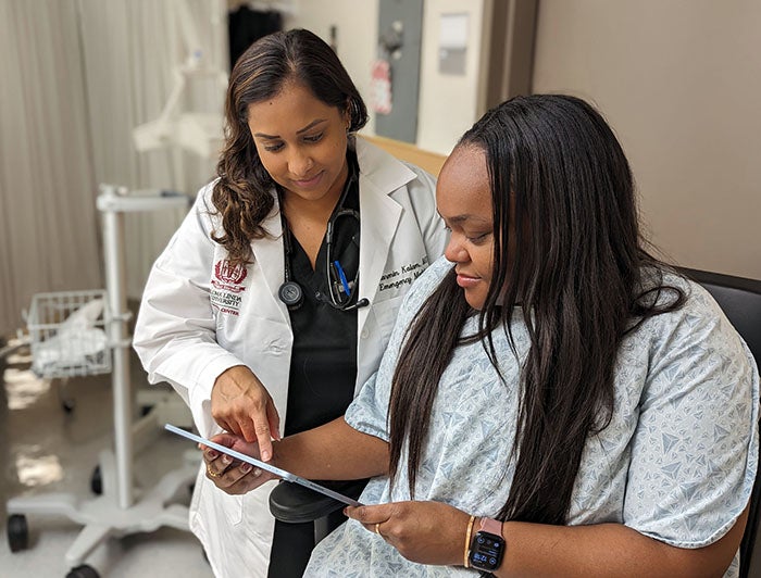 Loma Linda University Medical Center. Female clinician in white coat stands reviewing a tablet with a female patient in hospital gown.