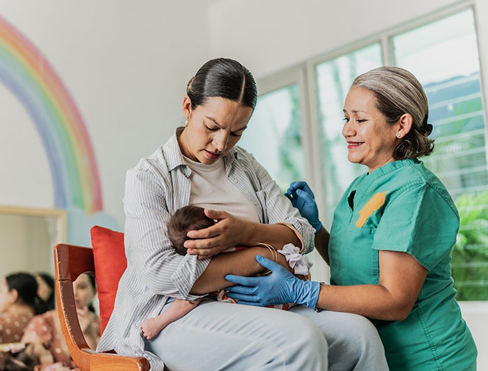 OSF Healthcare. A nurse midwife in scrubs helps a woman attend to her infant