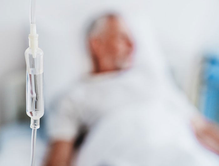 Fred Hutchinson Cancer Center. Blurred male patient sits in a hospital bed in background, IV drip in focus in foreground