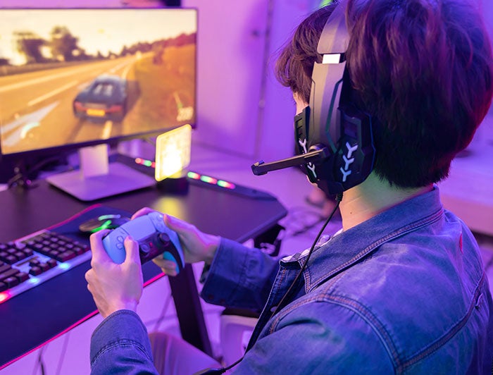 Mayo Clinic. Photo of a young man sitting at a gaming PC wearing a headset and holding a game controler