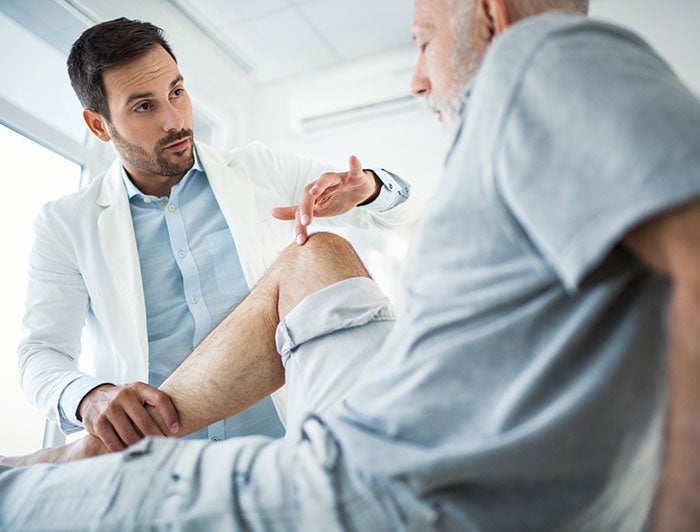 Copley Hospital. Copley Hospital. Physician and patient, both male, talking in a room while the physician holds patient's ankle and touches his knee