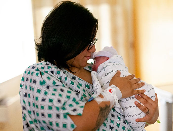 Sentara Northern Virginia Medical Center. Stock image of a new mother in hospital gown cradling her newborn