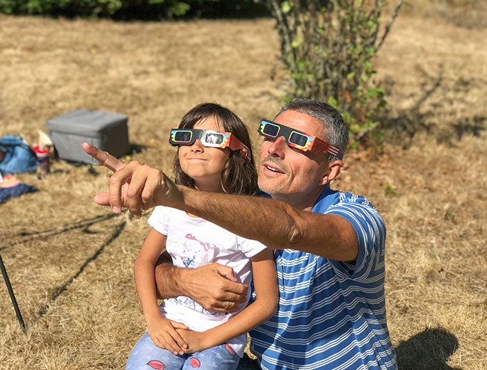 Saint Vincent Hospital Rochester Regional Health Rochester General Hospital. A man and child sitting outside wearing exlipse glasses look up at the eclipse