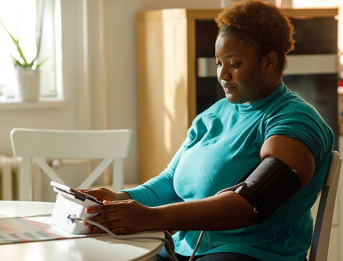 Rutland Regional Medical Center. A woman sits at her kitchen table checking her blood pressure with a home monitor