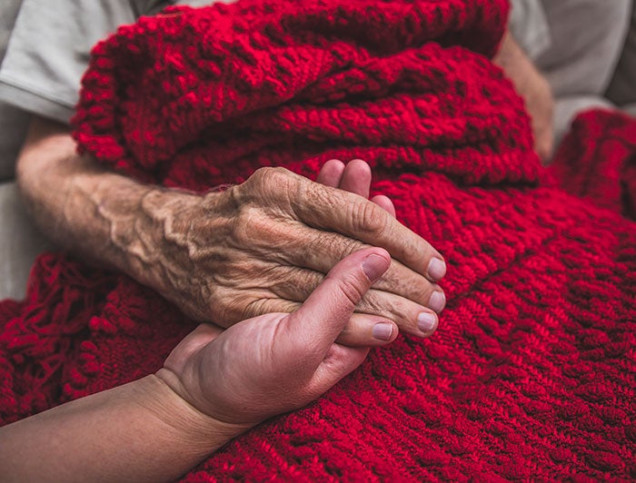 Mon Health Medical Center. stock image of a young carer's hands holding an elderly patient's hand.