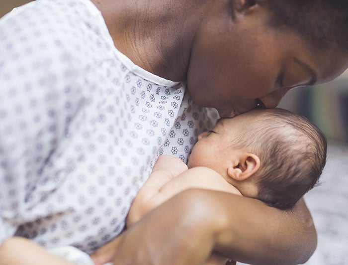 Dartmouth Health. A new mother in hospital gown kisses her newborn.