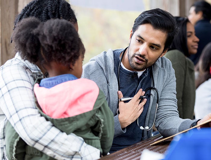Penn State Health. A male physician speaks with a little girl seated on her mother's lap at a rural clinic.