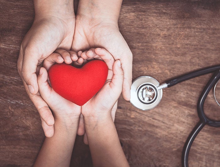 Kentucky Childrens. An adult health worker's hands, stretched across a table, shown holding the hands of a child holding a heart