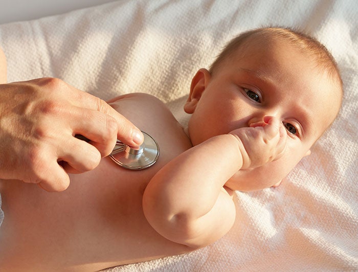 Norton Womens and Childrens Hospital. An infant rests on an exam table while a hand places a stethoscope against the infants chest.