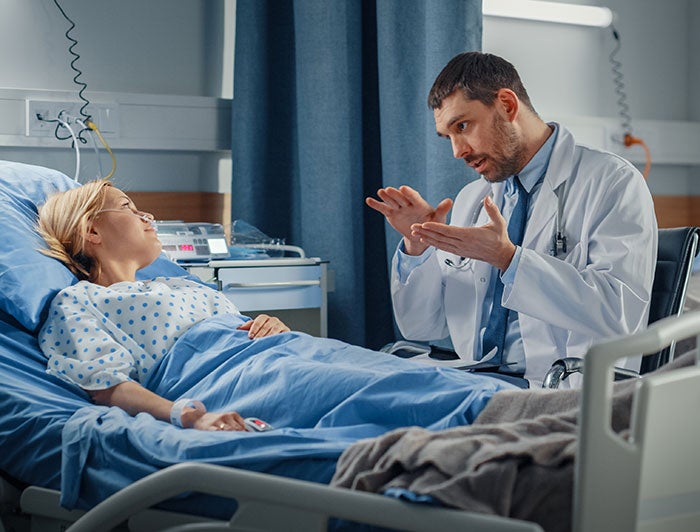 St. David’s Medical Center. Stock image shows a physician sitting at a patient bedside talking.