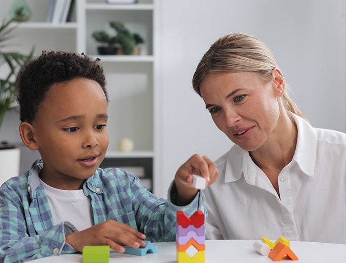 Intermountain Health. A young boy sits stacking blocks as a carer looks on