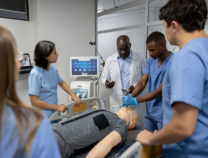 Baystate Health. A physician and a group of young trainees stand around a mannequin in a hospital bed