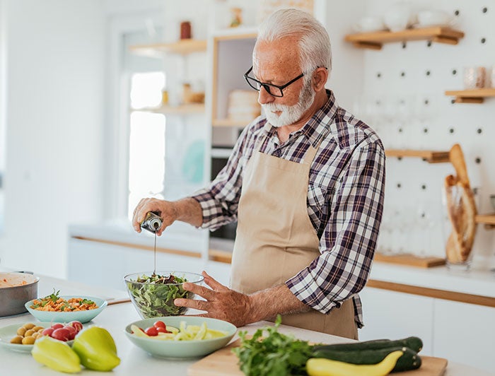 Cary Medical Center. An older man stands in a kitchen preparing a healthy meal of salad