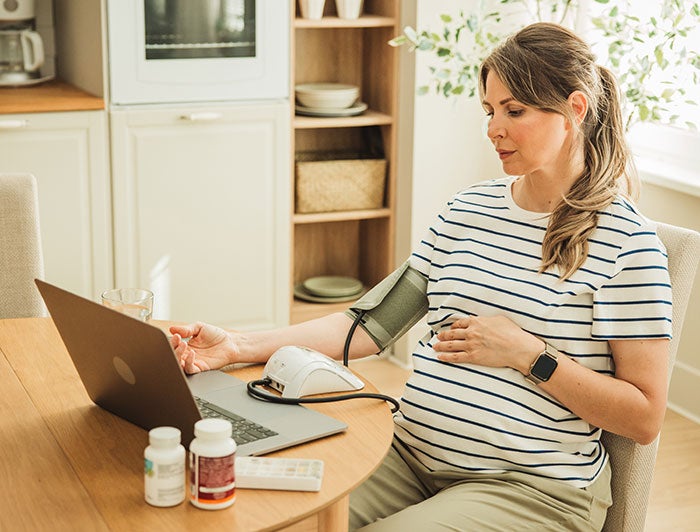 Evanston Regional Hospital. A pregnant woman sits at a kitchen table measuring her blood pressure and looking at a laptop