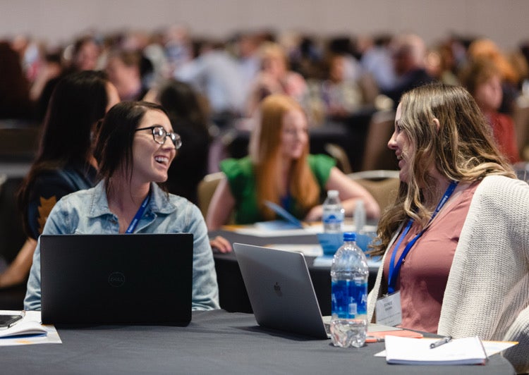 Two women are talking happily together in a conference room