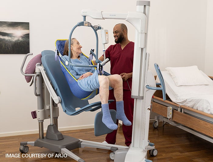 male nurse in scrubs helps female patient using a lift-assist device; image courtesy of ARJO