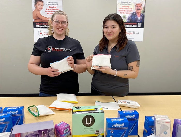 Arizona Diaper Bank participants stand at a table covered with packages of diapers and hygiene products