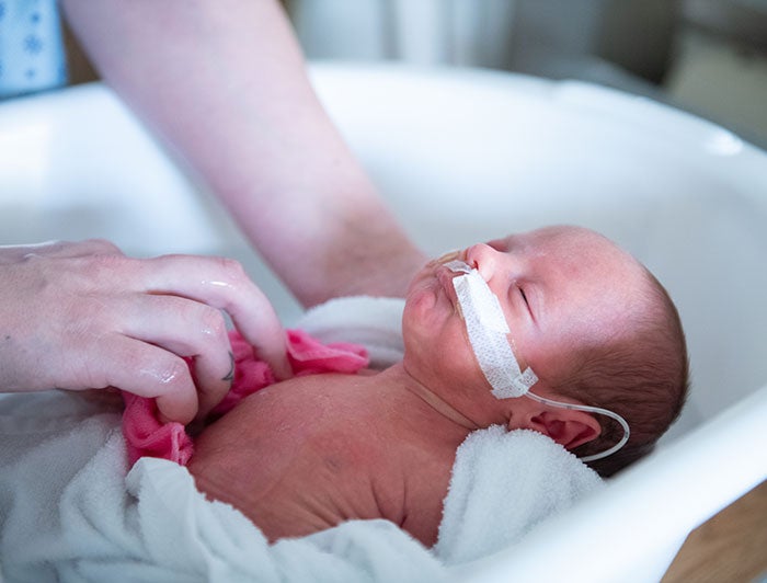 A NICU infant wrapped in towel gets a sponge bath