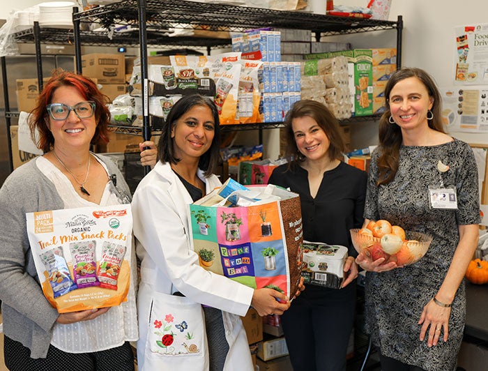 OHSU food pantry team members stand in front of pantry shelves holding packaged food