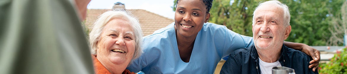 A group of older people sits outside talking with a health worker in scrubs