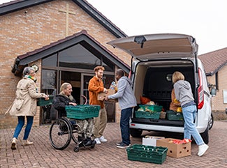 Volunteers unload donations from a van parked outside a church