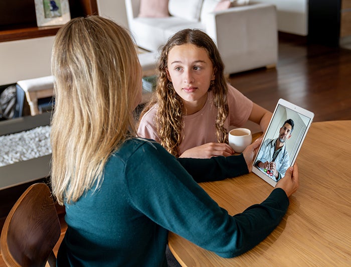 A woman and girl at home speak with a physician via tablet computer