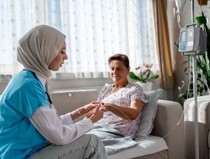 A health worker treats an older woman with an IV in her home