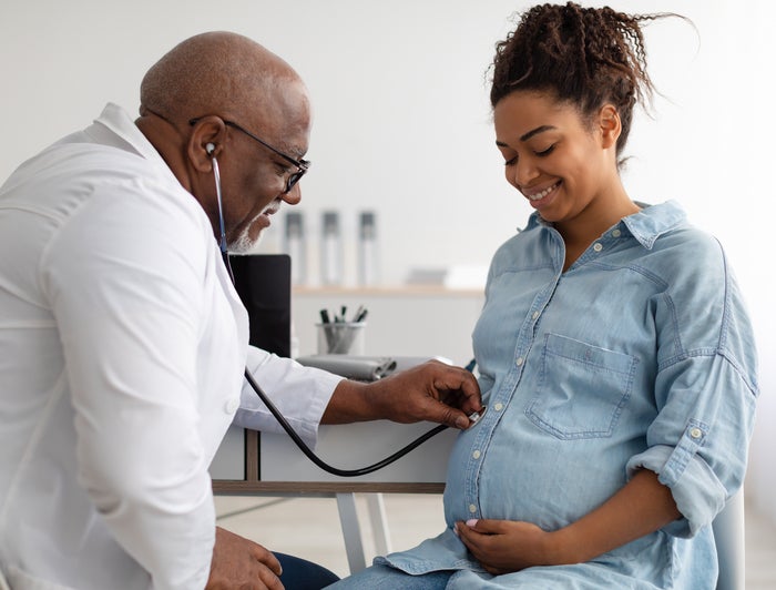 A doctor places a stethoscope on a pregnant woman's bump stomach